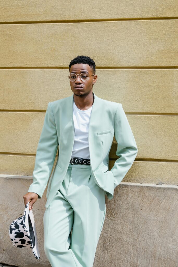 Fashion-forward man poses confidently in pastel suit against a textured wall.